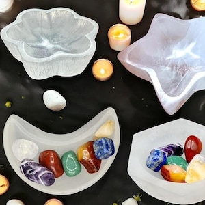 May include: Four white selenite bowls in different shapes, including a flower, a star, a crescent moon, and a hexagon. Each bowl is filled with colourful gemstones, including amethyst, red jasper, green aventurine, citrine, and lapis lazuli.