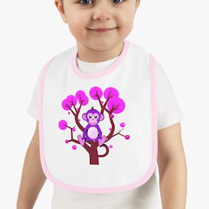 May include: A white baby bib with a pink trim features a purple monkey sitting in a pink tree with pink flowers.