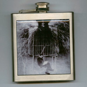 Könnte beinhalten: Eine silberne Trinkflasche mit einem Schwarzweißbild einer Person, die in einem Käfig sitzt, umgeben von Blitzen.