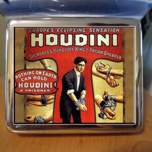 May include: A vintage-style poster advertising Houdini, "Europe's Eclipsing Sensation", with the text "The World's Handcuff King & Prison Breaker". The poster features a red background with a black and white image of Houdini in a suit, with his hands bound in chains. The text "Nothing on Earth Can Hold Houdini A Prisoner" is also featured on the poster.