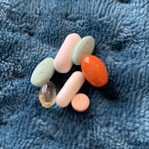 May include: A collection of various pills and capsules in different colors, including white, orange, light blue, and light green, on a blue fuzzy surface.