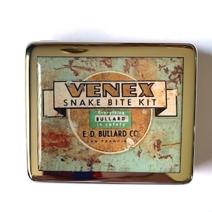 Pode incluir: Uma caixa de metal prateada com uma imagem vintage de um kit para picadas de cobra. A imagem apresenta o texto "VENEX SNAKE BITE KIT" e "E.D. BULLARD CO. SAN FRANCISCO".