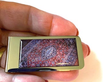 May include: A gold-toned money clip with a rectangular design. The clip features a colorful image of a patterned rug.