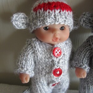 Puede incluir: Una mu&ntilde;eca de punto gris que lleva un gorro de punto gris y rojo con un pomp&oacute;n rojo. La mu&ntilde;eca tiene botones rojos en su atuendo.