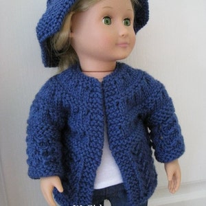 May include: A blue knitted cardigan with a cable knit pattern, worn by a doll with blonde hair and green eyes. The doll is also wearing a blue knitted hat and blue jeans. The text "WeGirls" is visible on the bottom of the image.