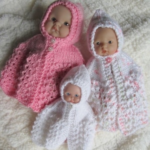 Peut inclure: Trois tenues de poupée en tricot rose et blanc avec des détails en crochet. Les tenues sont dotées de capuches et de fermetures à boutons.
