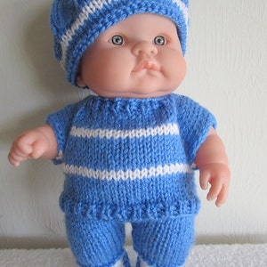 Puede incluir: Un conjunto de punto a rayas azul y blanco para una muñeca bebé. El conjunto incluye un gorro, un jersey y un pantalón.
