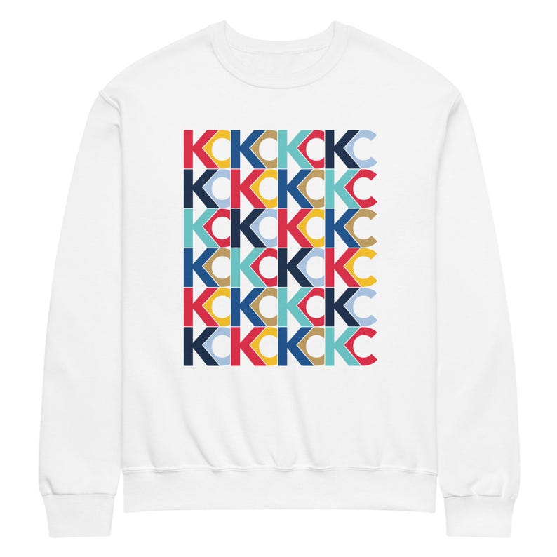 May include: White sweatshirt with a repeating pattern of the letters "KCKC" in a variety of colours, including red, blue, yellow, and teal. The design is centred on the front of the crew neck sweatshirt.
