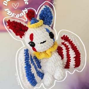 Peut inclure: Une chauve-souris blanche au crochet avec des accents rouges, bleus et jaunes. La chauve-souris a un design de clown avec un chapeau pompon rouge, des ailes bleues et rouges et des yeux noirs. Le texte sur l'image indique "Fichier numérique PDF uniquement."
