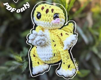 May include: A crocheted yellow and white gecko with brown spots and a pink tongue. The gecko is outlined in white and the text "Digital file PDF only" is in a circular design above the gecko.