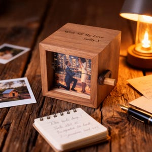 May include: A wooden photo cube displaying a proposal scene. The cube is engraved with "With All My Love Sally X". A small notepad and pen are placed nearby. The cube sits on a wooden surface, with other items in the background.