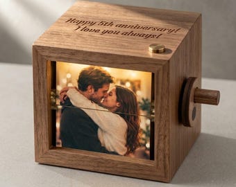 May include: A square wooden music box featuring a photo of a couple embracing on the front panel. The top surface is engraved with the text Happy 5th anniversary! I love you always! A small circular wooden crank handle is attached to the right side.