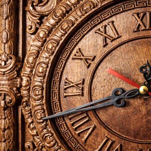 May include: Close-up of a wooden clock with Roman numerals. The clock face is a warm brown color, with ornate carvings around the edge. The hands are black, with a red second hand and a gold center.