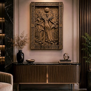 May include: A detailed, brown relief carving of a woman with outstretched arms, framed by a decorative border, hangs on a wall. The carving is above a dark wood cabinet with gold accents. A black vase and other decor are on the cabinet.
