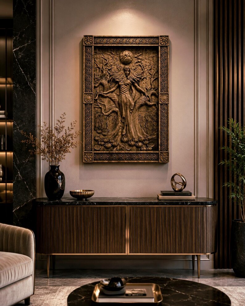 May include: A detailed, brown relief carving of a woman with outstretched arms, framed by a decorative border, hangs on a wall. The carving is above a dark wood cabinet with gold accents. A black vase and other decor are on the cabinet.