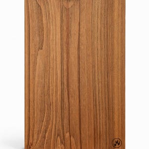 May include: A rectangular wooden board with a warm brown finish and vertical wood grain. A brass sawtooth hanger is attached to the top. A small circular logo is in the bottom right corner.