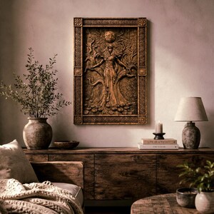 May include: A detailed, brown wooden wall art piece depicting a figure with outstretched arms, surrounded by trees and a sun. The art is framed and mounted on a neutral-toned wall, above a wooden cabinet. A lamp, books, and a candle are also visible.