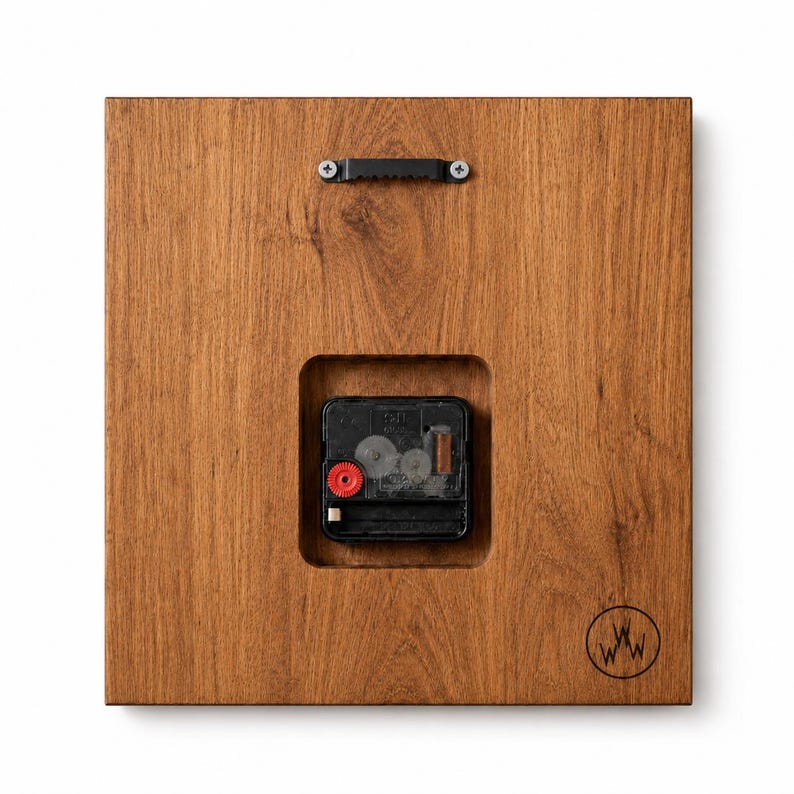 May include: Back of a square wooden clock with a visible clock mechanism. The wood has a warm brown tone. A black metal hanger is attached at the top, and the clock mechanism is visible in a recessed square. A logo is in the bottom right corner.