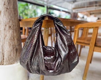 May include: A dark brown hobo bag with a textured snakeskin pattern. The bag features a slouchy, unstructured silhouette with a single integrated shoulder strap and a deep, curved opening. The material has a subtle metallic sheen throughout.
