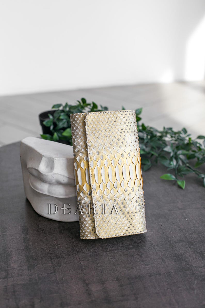 Slim women's python wallet closed, showcasing the metallic gold finish under natural light.