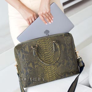 May include: A green snakeskin-patterned leather handbag with a black strap and gold hardware. The bag is open and a silver laptop computer is inside.
