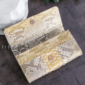 Gold and white snakeskin wallet with a snap closure. The wallet is open and the interior is visible.