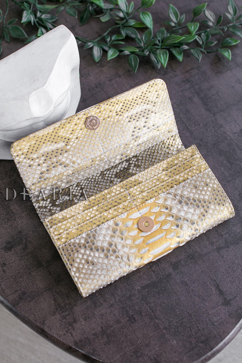 Gold and white snakeskin wallet with a snap closure. The wallet is open and the interior is visible.