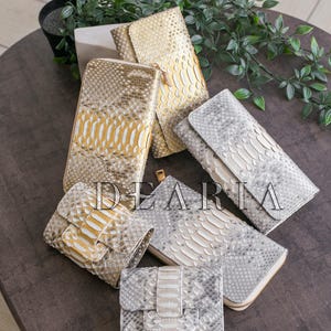 A collection of different snakeskin wallets in various shades of gold and silver.