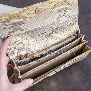 A beige and gold snakeskin wallet with a zippered compartment and multiple card slots. The wallet is open and the interior is visible.