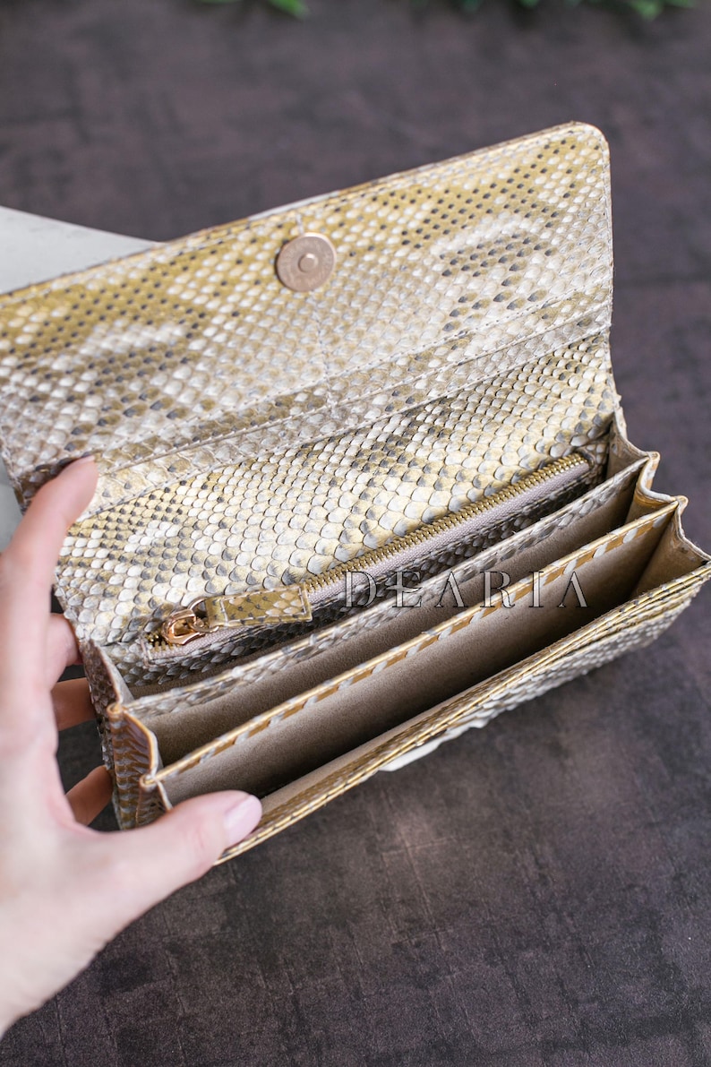 A beige and gold snakeskin wallet with a zippered compartment and multiple card slots. The wallet is open and the interior is visible.