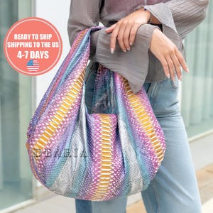 May include: A colorful, patterned handbag with a unique design. The bag features a blend of yellow, purple, and blue hues, creating a vibrant and eye-catching appearance. The word "DEARIA" is visible on the bag. This stylish accessory is perfect for carrying essentials.