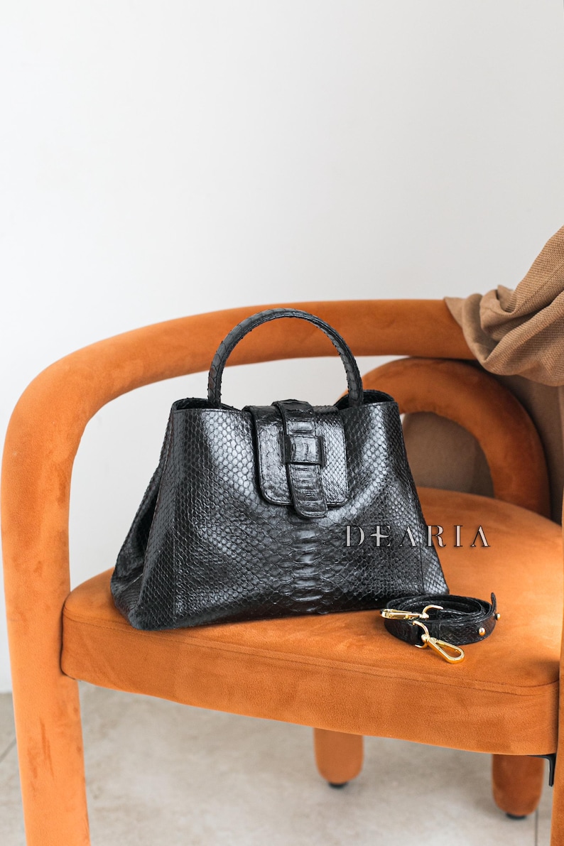 Black snakeskin python leather handbag with a magnetic flap closure and shoulder strap.