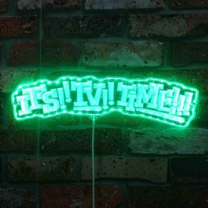 以下が含まれることがあります： 白いブロック体の文字で「IT'S TIME!!」と書かれたネオングリーンのサイン。サインは明るい緑色の光で縁取られ、レンガの壁に取り付けられています。サインは点灯しており、表示する準備ができています。