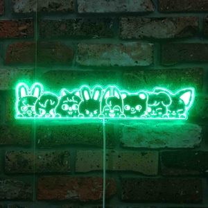 May include: A neon green light fixture featuring a row of cartoon animal faces, including a bunny, cat, and bear, against a brick wall background. The light is emitting a bright green glow, creating a playful and whimsical aesthetic.