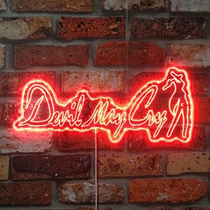 Puede incluir: Un letrero de neón rojo con las palabras "Devil May Cry" en una fuente estilizada. El letrero también presenta una silueta de una mujer en una pose sugerente.