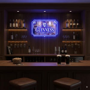 Può includere: Un'insegna al neon blu con il logo Guinness illumina un bar domestico. L'insegna è incorniciata e montata su una parete di legno. Il bar presenta scaffali con bottiglie e bicchieri. Due pinte di Guinness sono sul bancone.