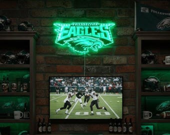 May include: A neon green Philadelphia Eagles sign is mounted on a brick wall above a television. The TV displays a football game. Shelves on either side hold Eagles-themed merchandise, including helmets and mugs. A team flag is visible.