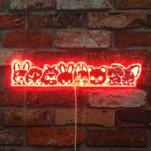 May include: A red neon light fixture featuring a row of cartoon animal faces, including a rabbit, bear, and dog. The light is mounted on a brick wall. The fixture is a decorative item.