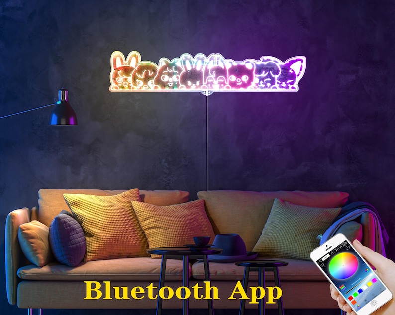 May include: A colorful LED light fixture shaped like a row of cartoon animals. The light is mounted on a wall above a sofa. The words "Bluetooth App" are displayed in yellow text at the bottom of the image. A smartphone displays a color wheel.