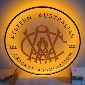 Może przedstawiać: Okrągły, podświetlany znak z napisem "WESTERN AUSTRALIAN CRICKET ASSOCIATION" w okręgu. Znak zawiera centralne logo i rok "1885". Znak emituje ciepłą, ż&oacute;łtą poświatę.