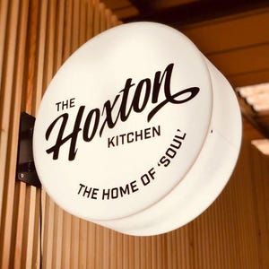 Op de afbeelding: Wit verlicht bord met zwarte tekst die "The Hoxton Kitchen, The Home of 'Soul'" luidt.