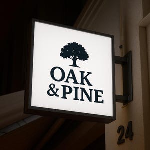 K&ouml;nnte beinhalten: Quadratisches, beleuchtetes Schild mit dem Text "OAK & PINE" in fetter, dunkler Schrift, dar&uuml;ber eine Baumsilhouette. Das Schild ist an einer dunklen Metallhalterung an einer neutralen Wand befestigt. Die Nummer "24" ist darunter sichtbar.