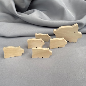 May include: A collection of six wooden pig figurines in various sizes. The pigs are unpainted, showcasing the natural wood grain. Each pig has a simple, rounded design with small details for eyes and snouts. The largest pig measures approximately 4 inches long.