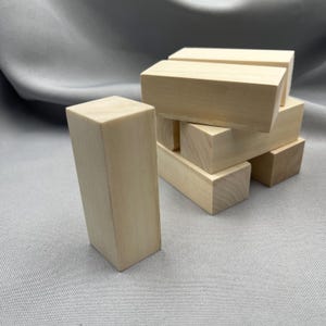 May include: A collection of unfinished wooden blocks, ideal for crafts or construction. The blocks are rectangular and have a light, natural wood colour. Some blocks are stacked, while others stand alone.