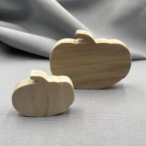 Könnte beinhalten: Zwei Kürbis-Ausschnitte aus Holz. Einer ist größer als der andere. Die Kürbisse sind aus hellem Holz gefertigt und haben eine natürliche Oberfläche. Die Kürbisse sind wahrscheinlich für Herbst- oder Halloween-Dekorationen.