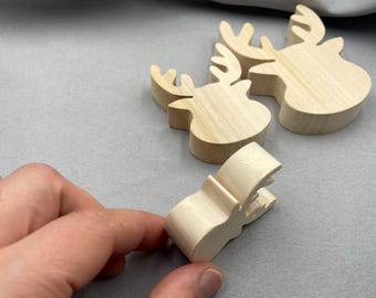 May include: Wooden moose head cutouts and a small wooden clip. The moose heads are light-colored with detailed antlers. The clip is also light-colored and has a curved shape. The items are on a gray surface.