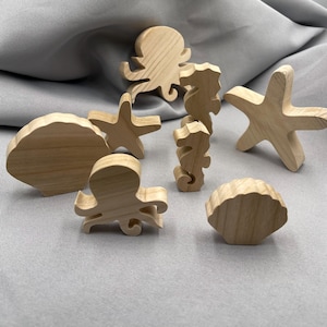 Könnte beinhalten: Eine Sammlung von Holz-Meereskreaturen, darunter ein Oktopus, Seestern, Seepferdchen und Muscheln. Die Holzspielzeuge sind hellbraun und haben eine natürliche Holzmaserung. Geeignet für Kinder zum Spielen und Lernen.