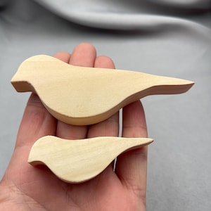 May include: Two wooden bird-shaped cutouts in natural wood color. One is larger than the other. The birds have a simple, rounded design with a beak and tail. They are likely intended for crafting or decoration.