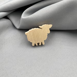 Pode incluir: Um elemento artesanal em forma de ovelha de madeira. A ovelha &eacute; castanha clara e tem um design simples e estilizado. Est&aacute; colocada sobre um fundo de tecido cinzento, criando uma est&eacute;tica neutra e natural. Ideal para projetos de artesanato.