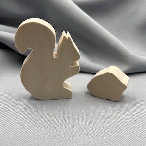May include: Two unfinished wooden squirrel cutouts. One is a full squirrel shape, and the other is a small, rounded shape. The squirrel is in a standing position with its tail curved. The wood is a light, natural color.